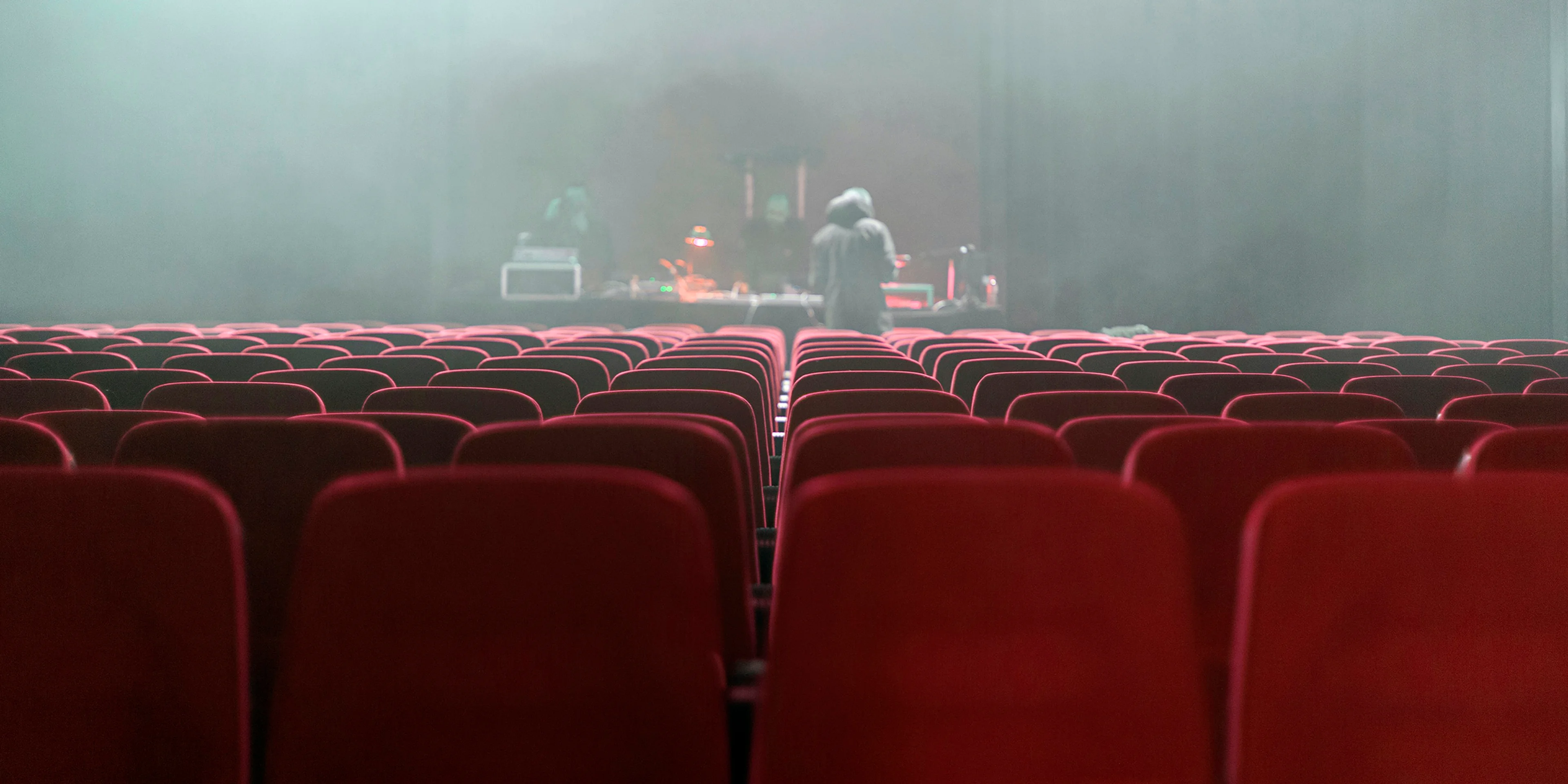 people sitting on red chairs watching a band performing on stage.
