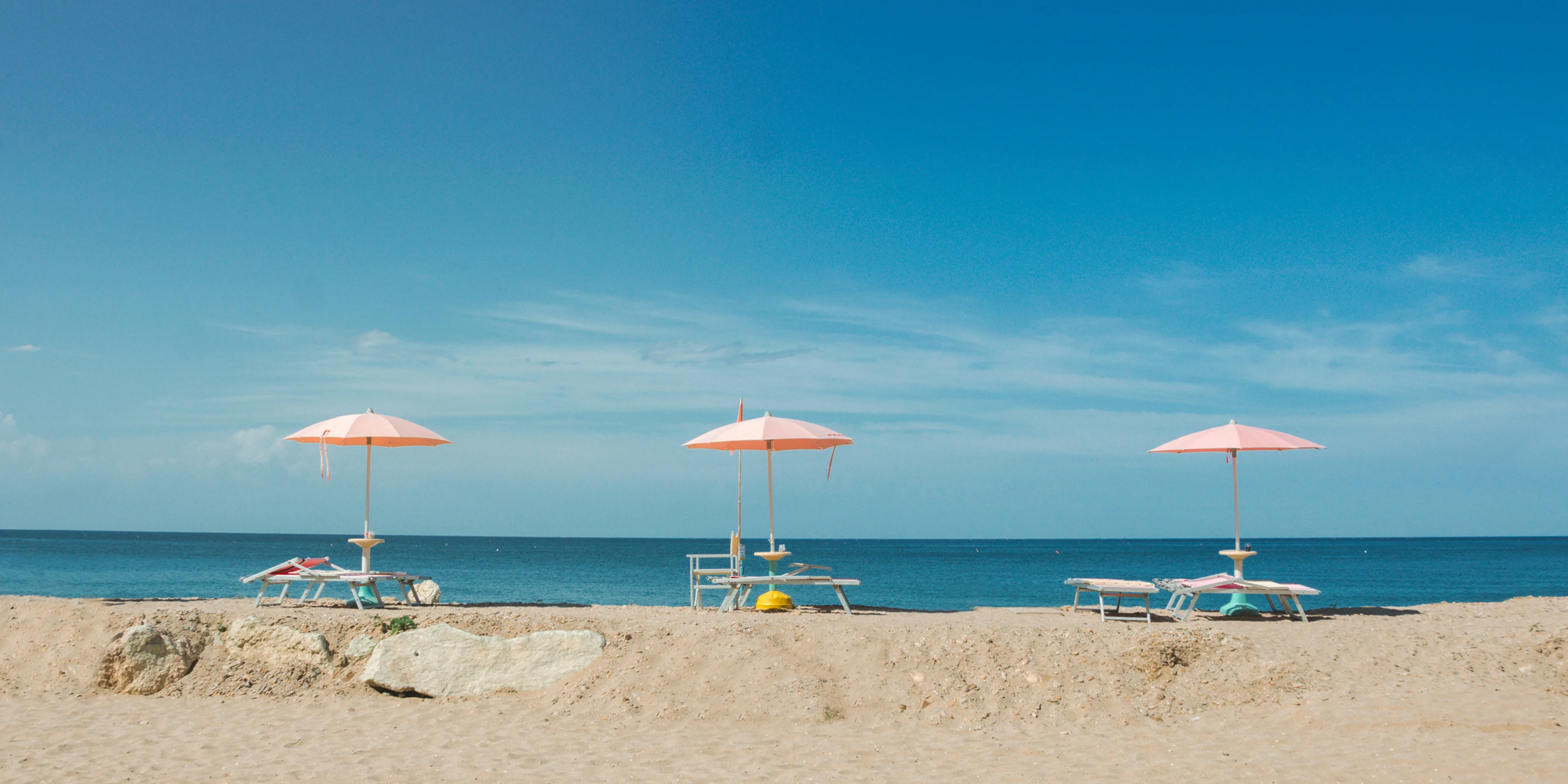 three empty beach loungers with umbrellas overlooking the beach under blue sky.