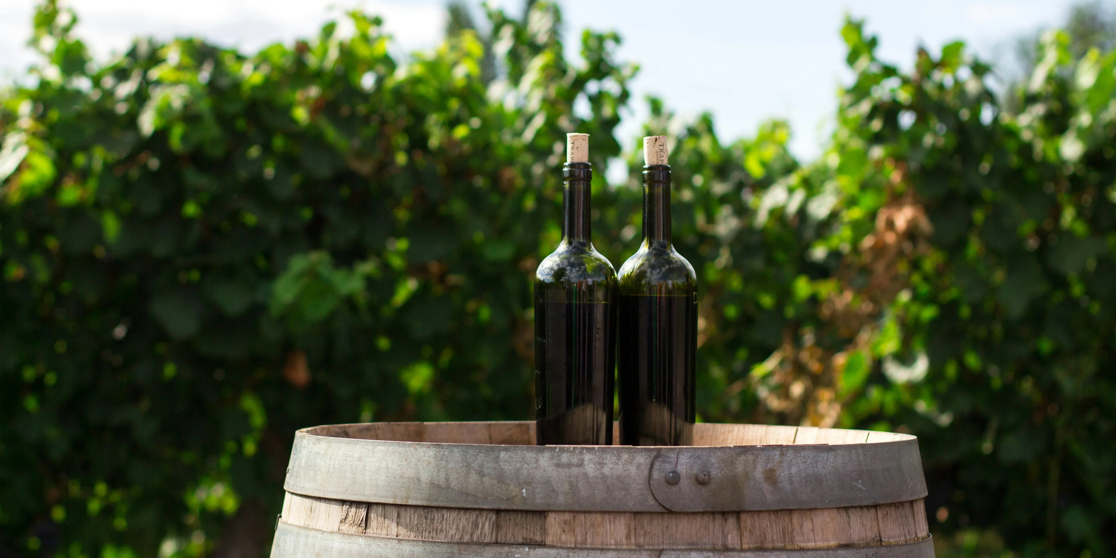two black glass bottles on the top of the brown wooden barrel.