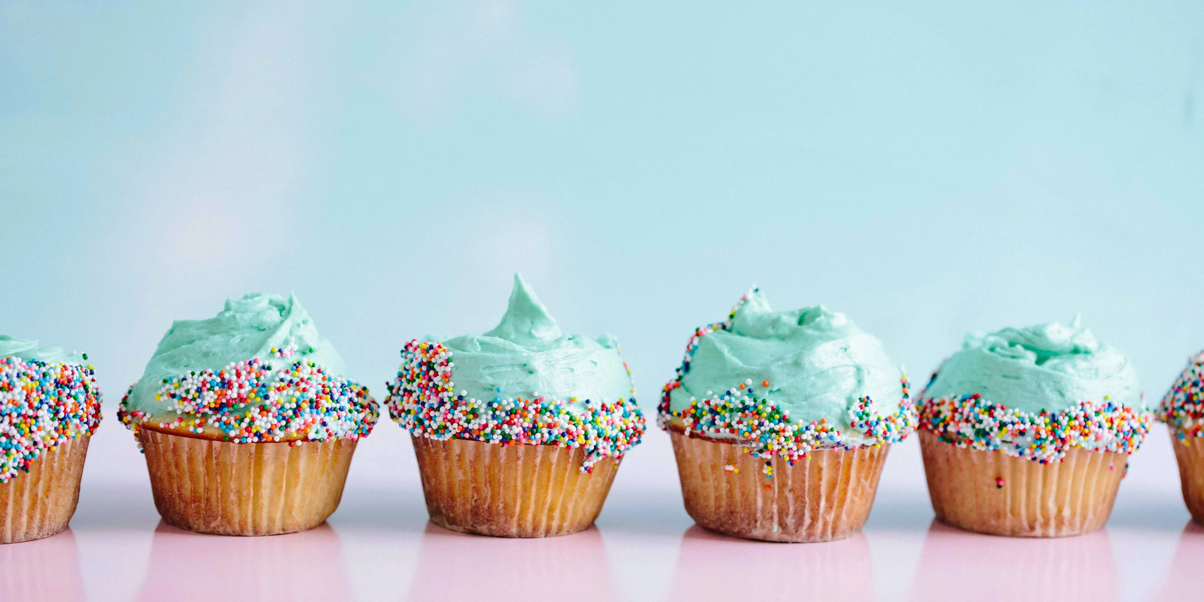 six teal icing cupcakes with sprinkles.