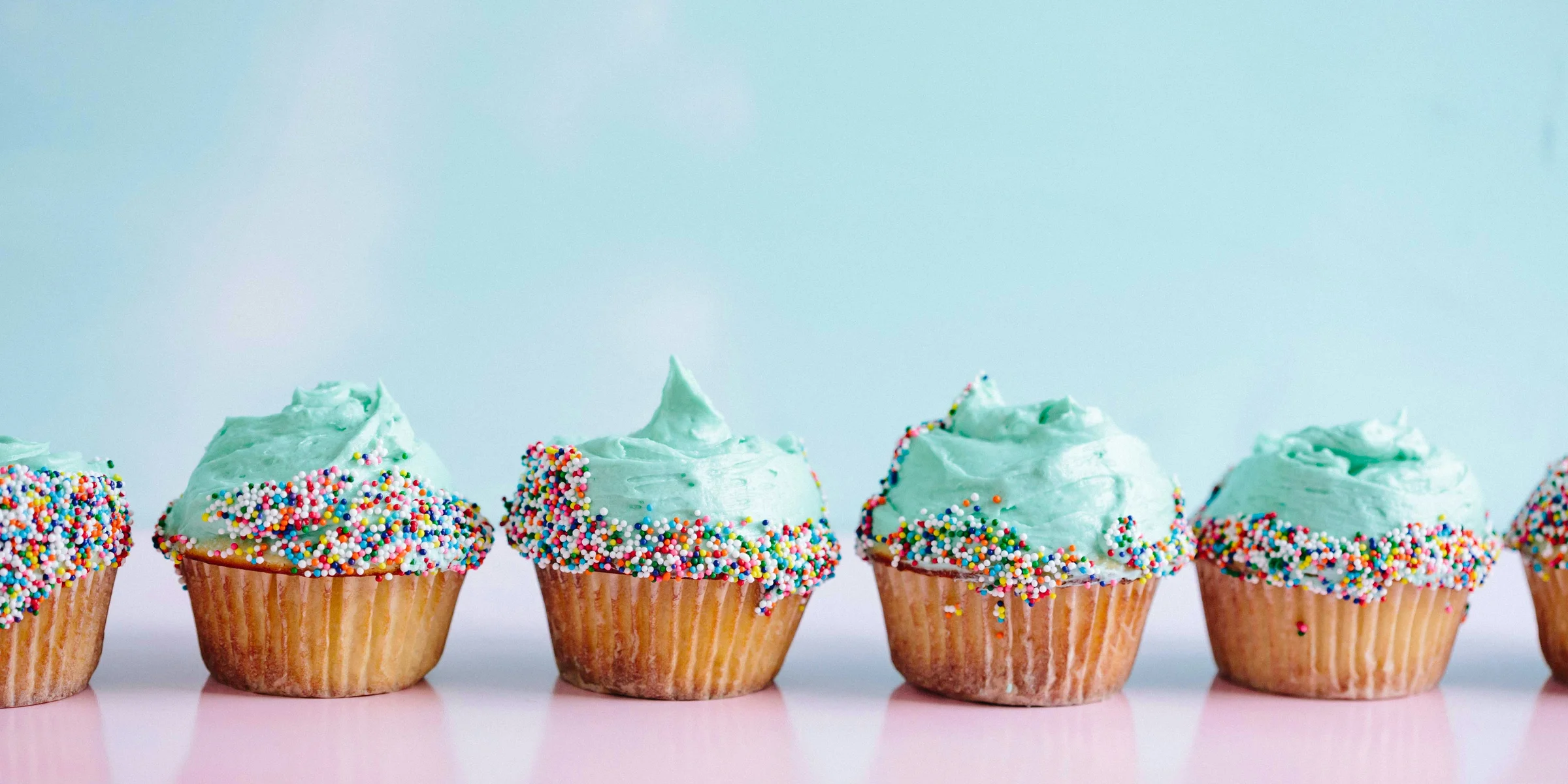 six teal icing cupcakes with sprinkles.