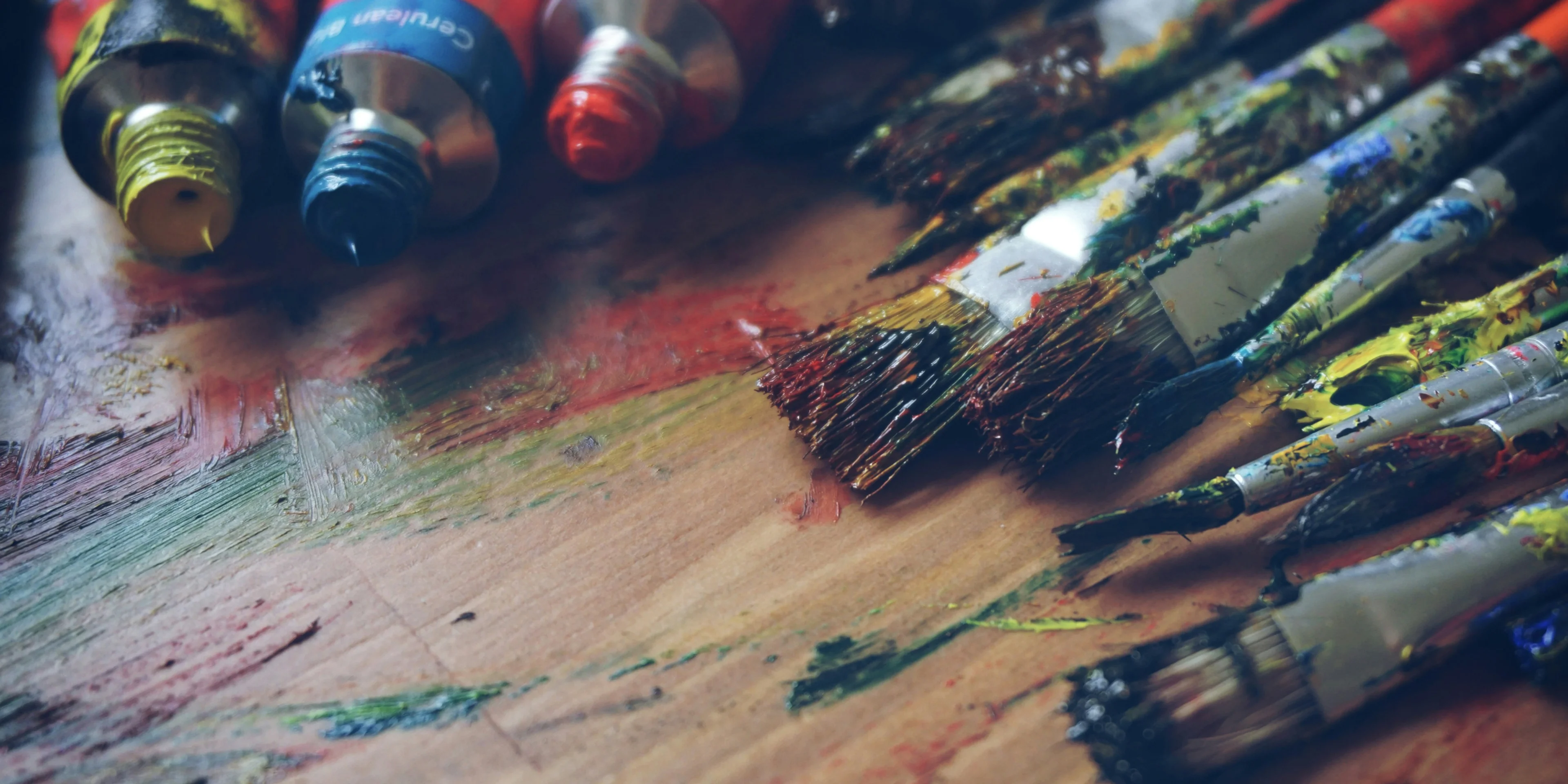 three paint tubes near paint brushes.