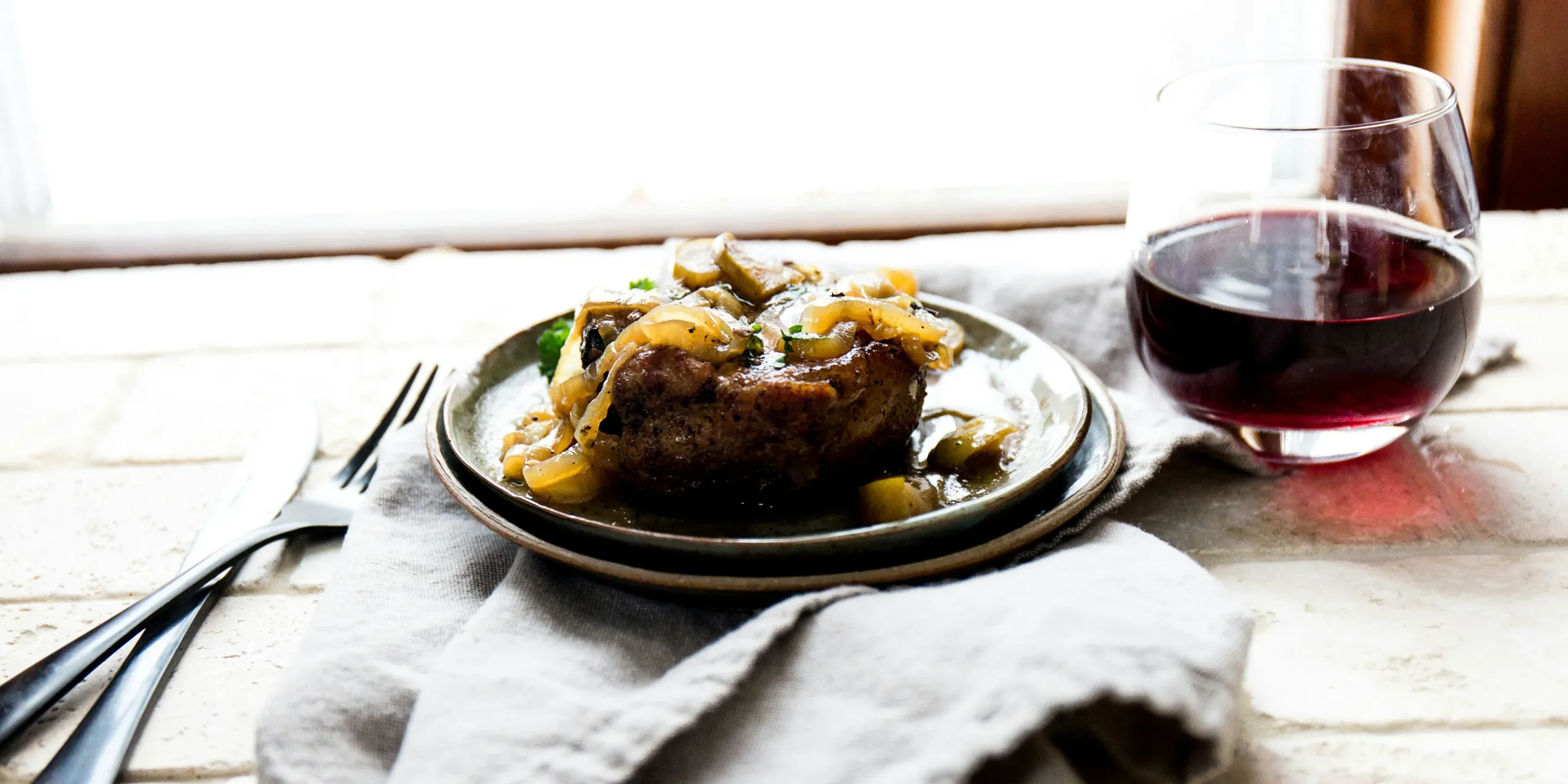 cooked food on ceramic plate beside wine glass and fork and cutlery knife on top of table