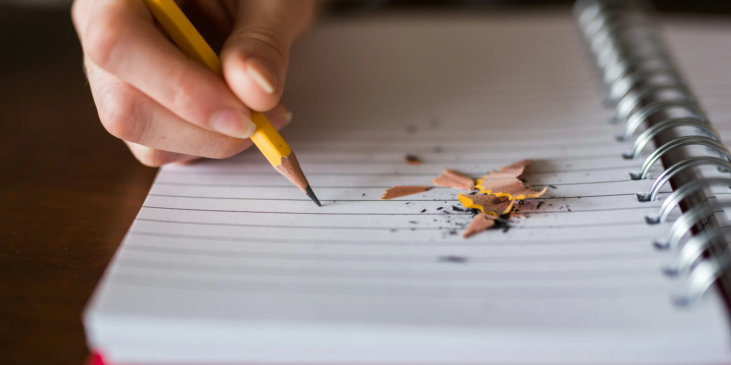 person holding pencil writing on notebook.