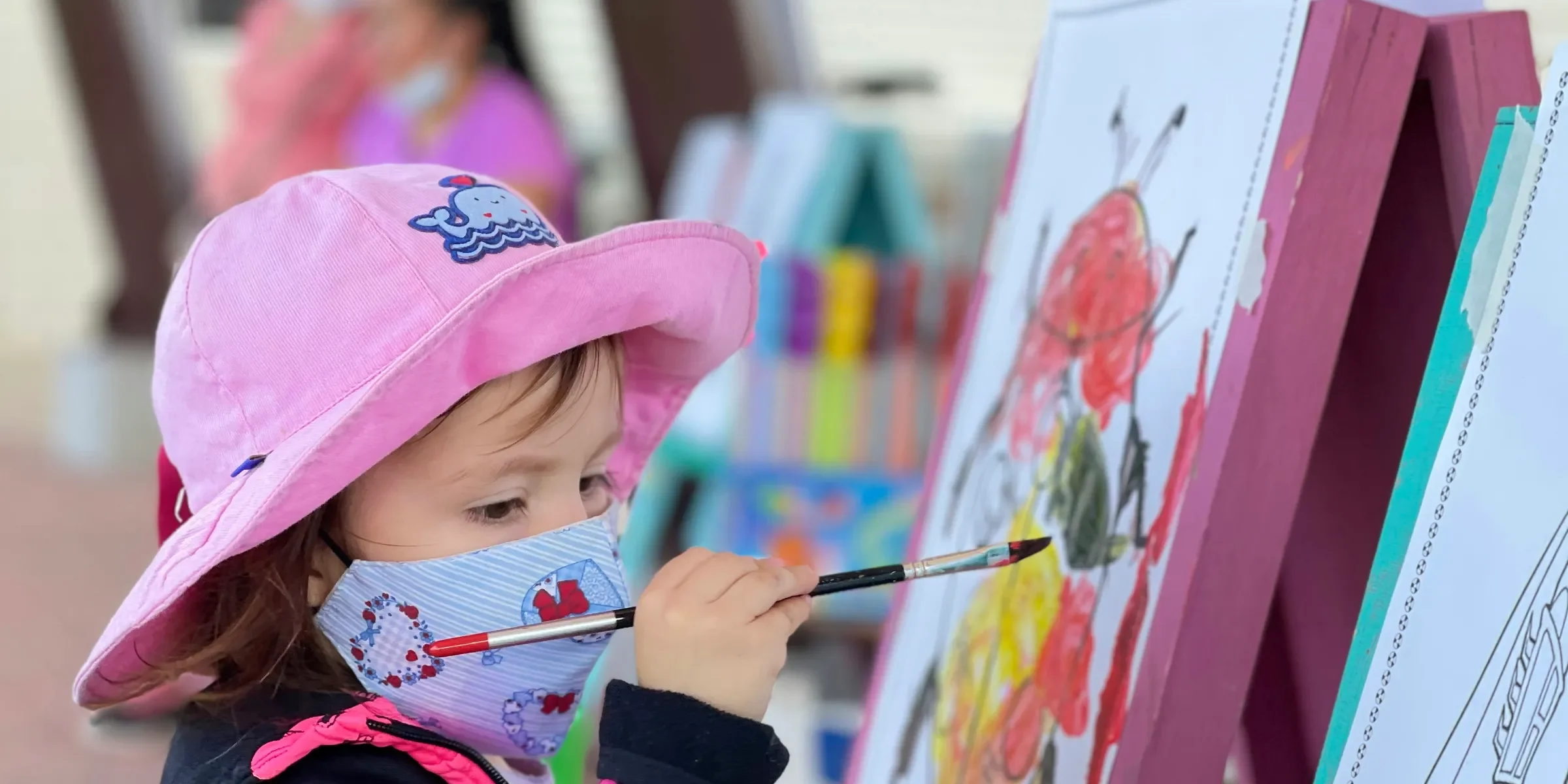 girl in pink cap and black jacket painting on white board