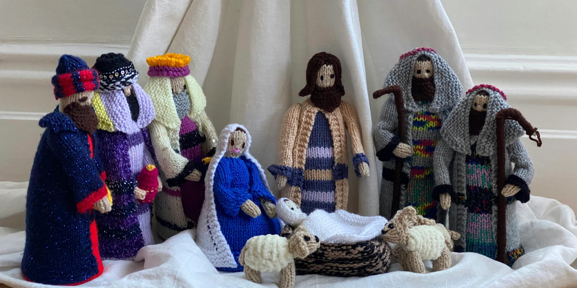 three white and blue knitted dolls on white textile.