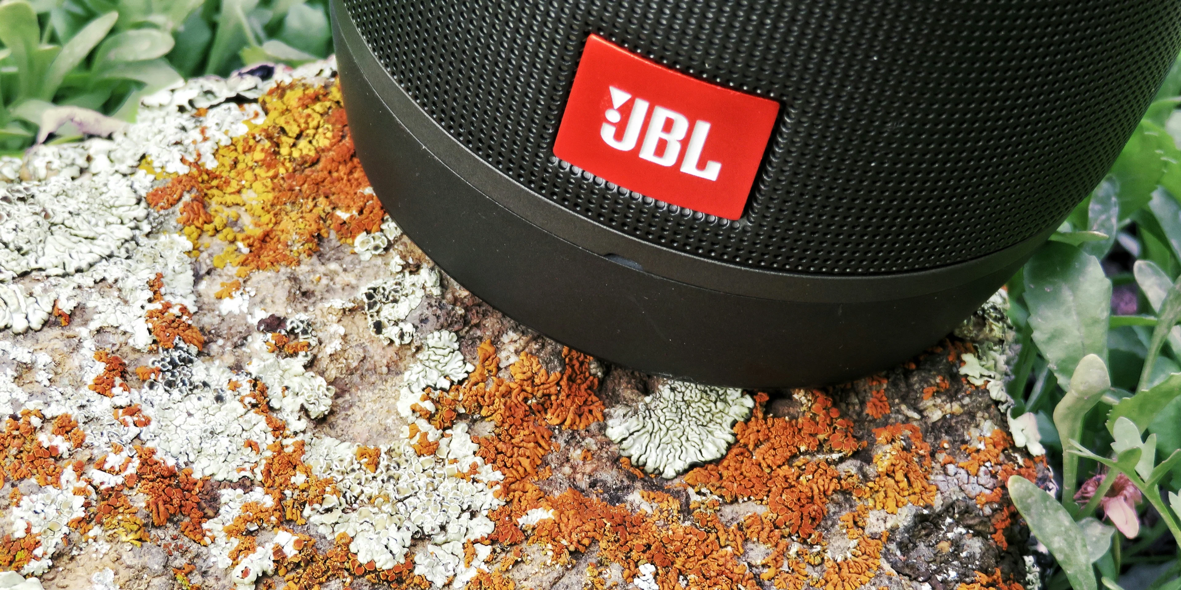 black jbl portable speaker on brown and white textile.