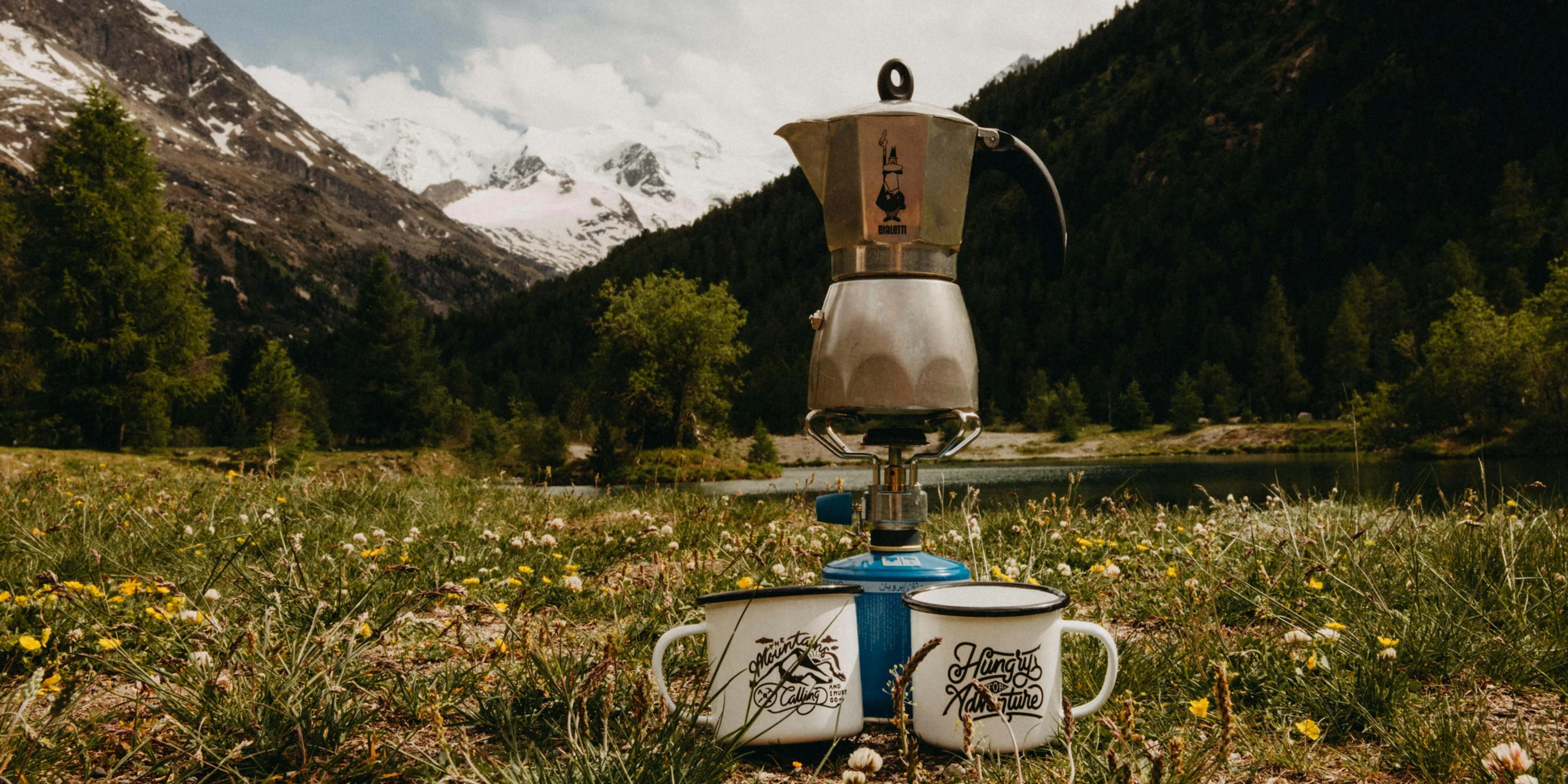 gray stainless steel mokapot on burner between two white mugs on green grass