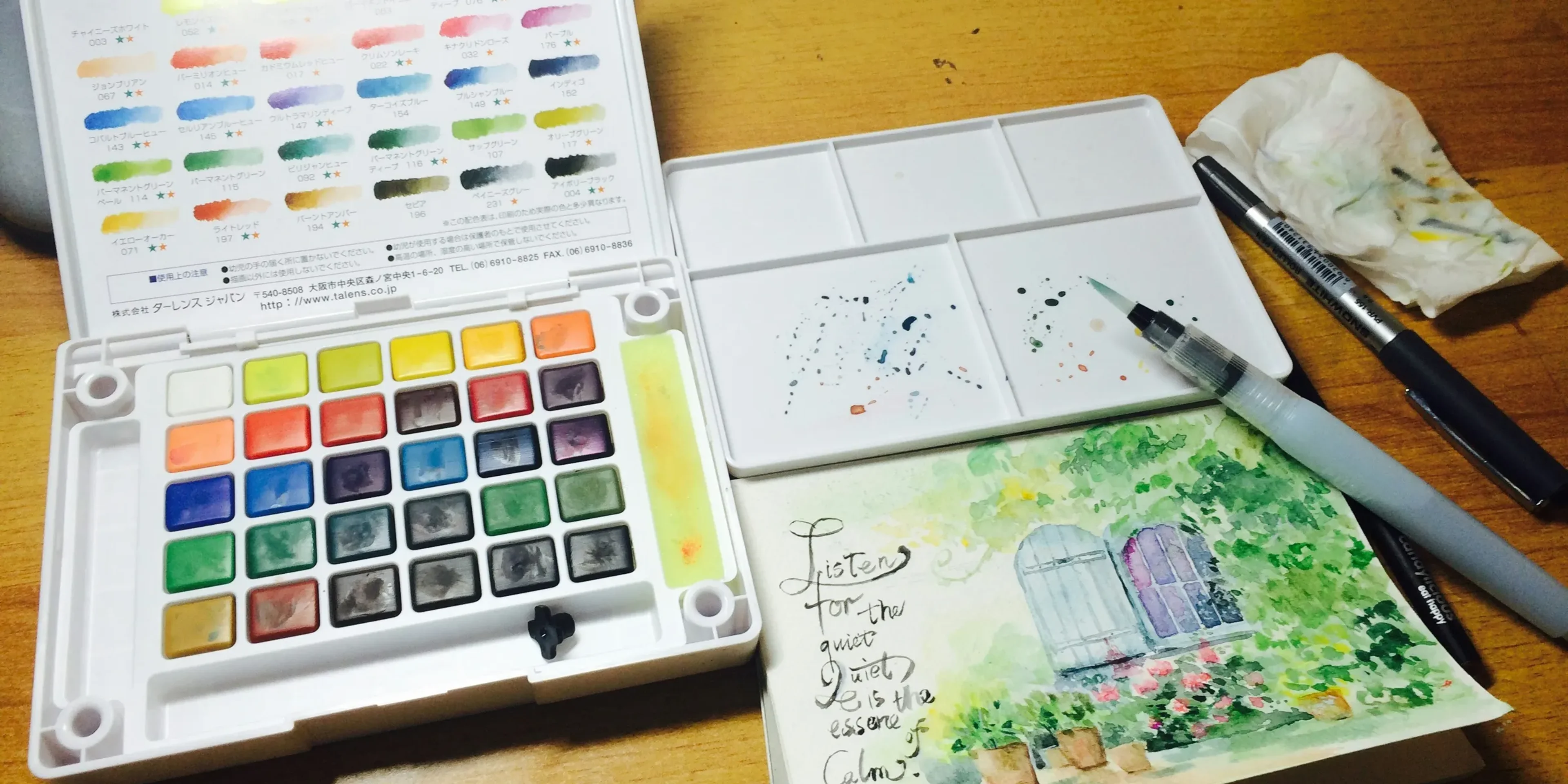 A wooden table topped with a white box filled with watercolors
