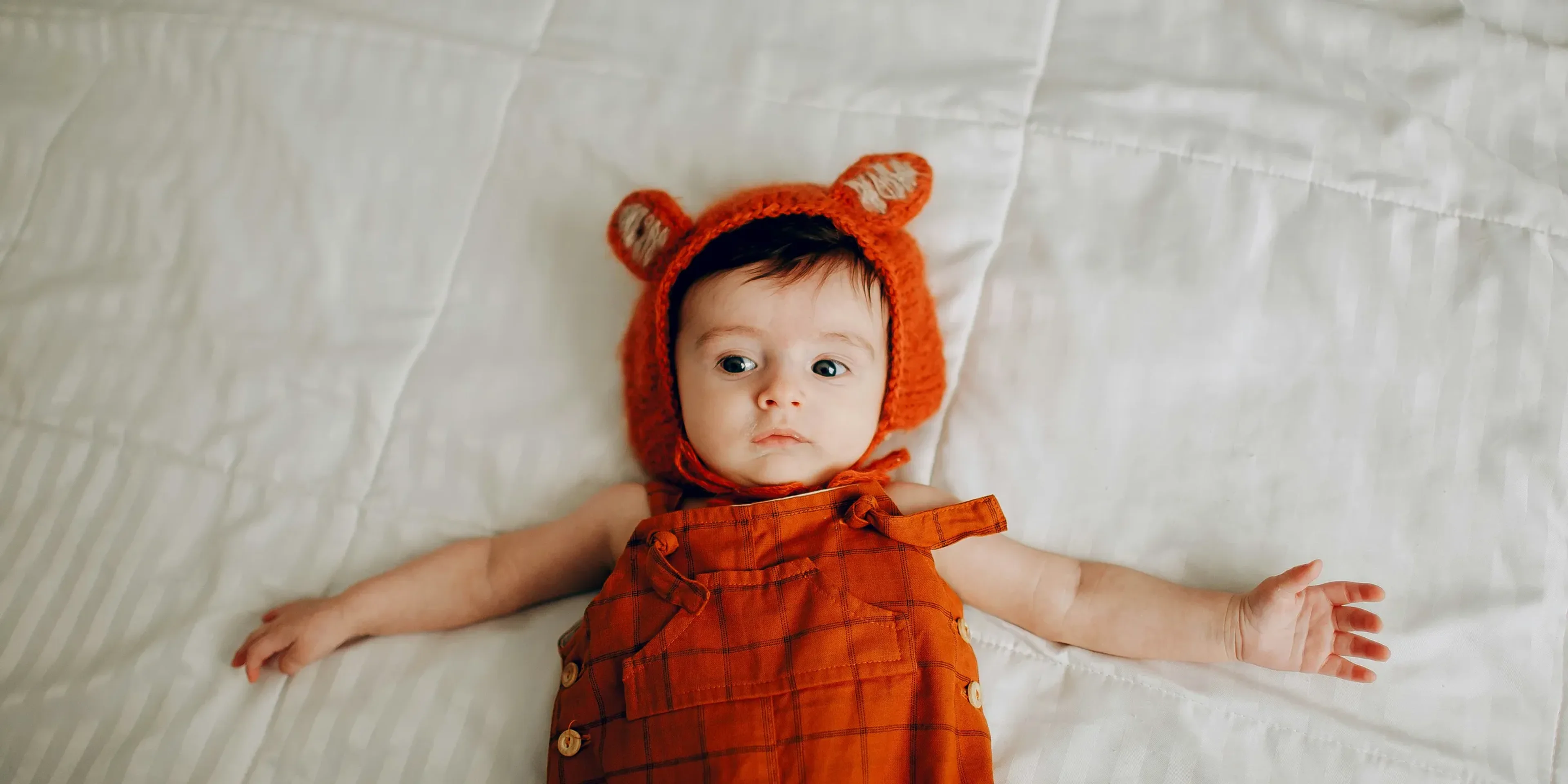 baby in red and black plaid dress lying on white bed