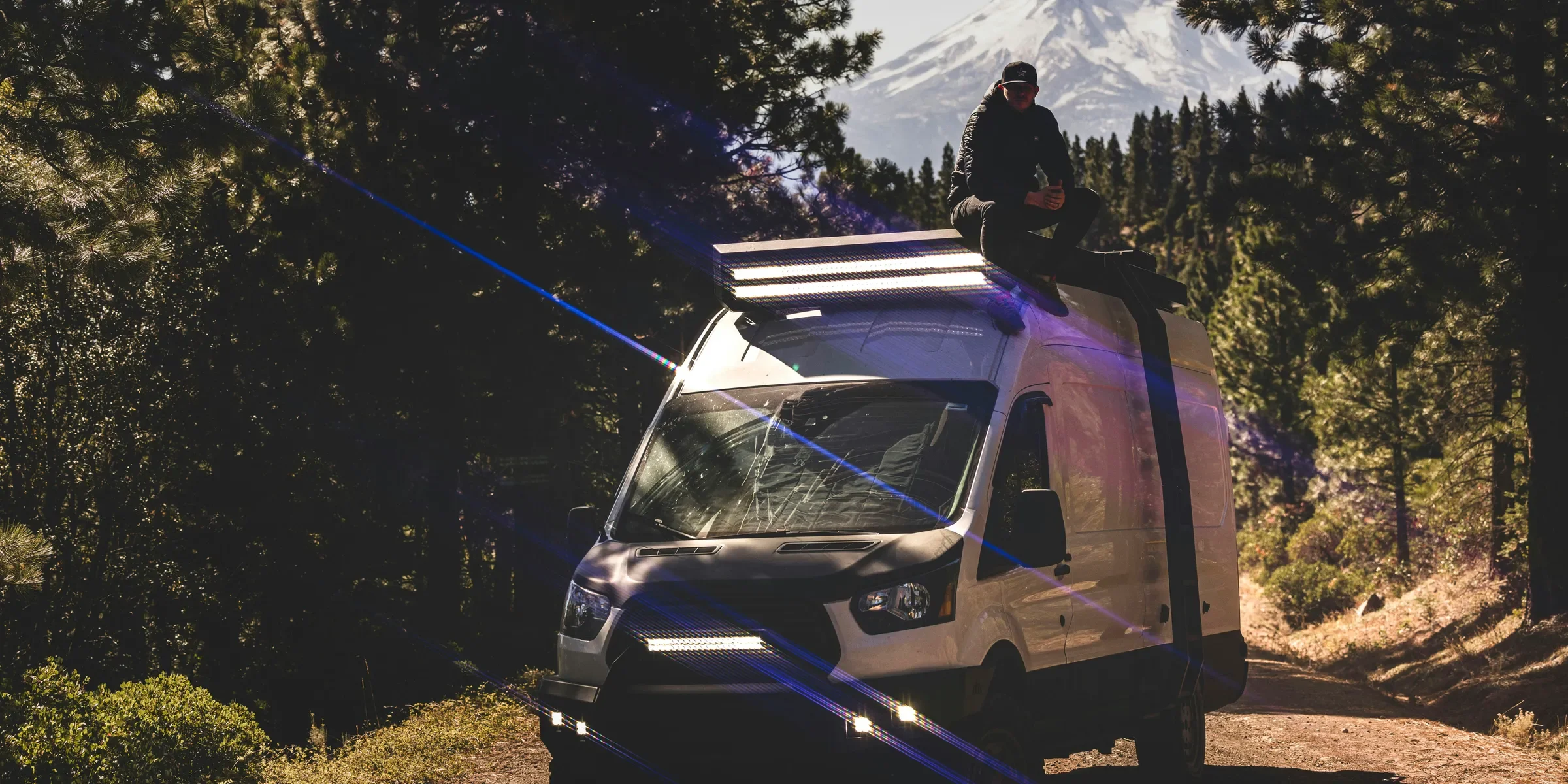 a man sitting on top of a van on a dirt road