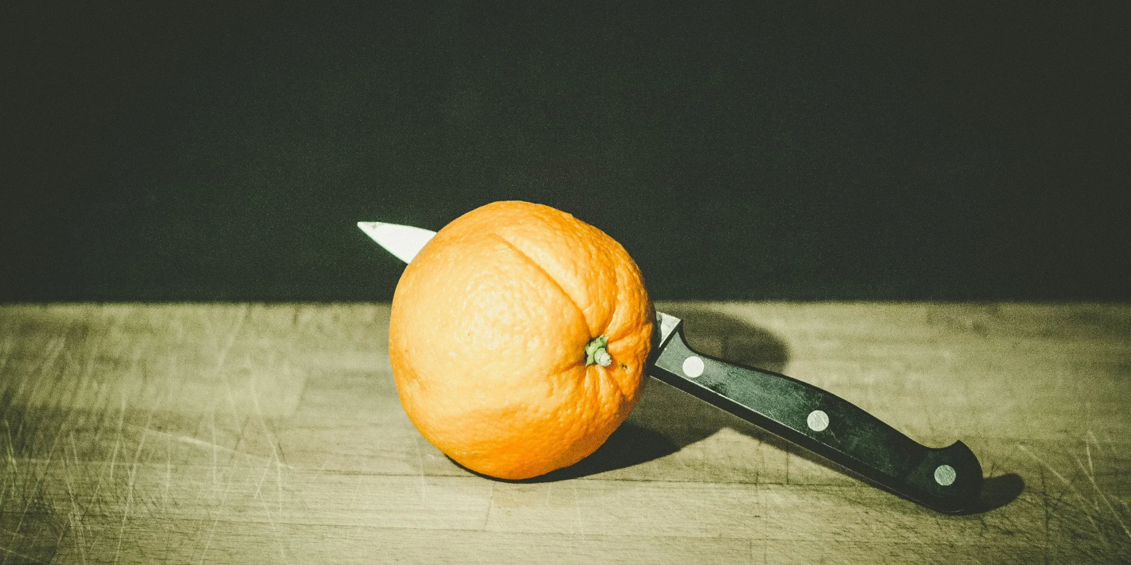 orange fruit and gray and black knife on brown wooden board low-light photography