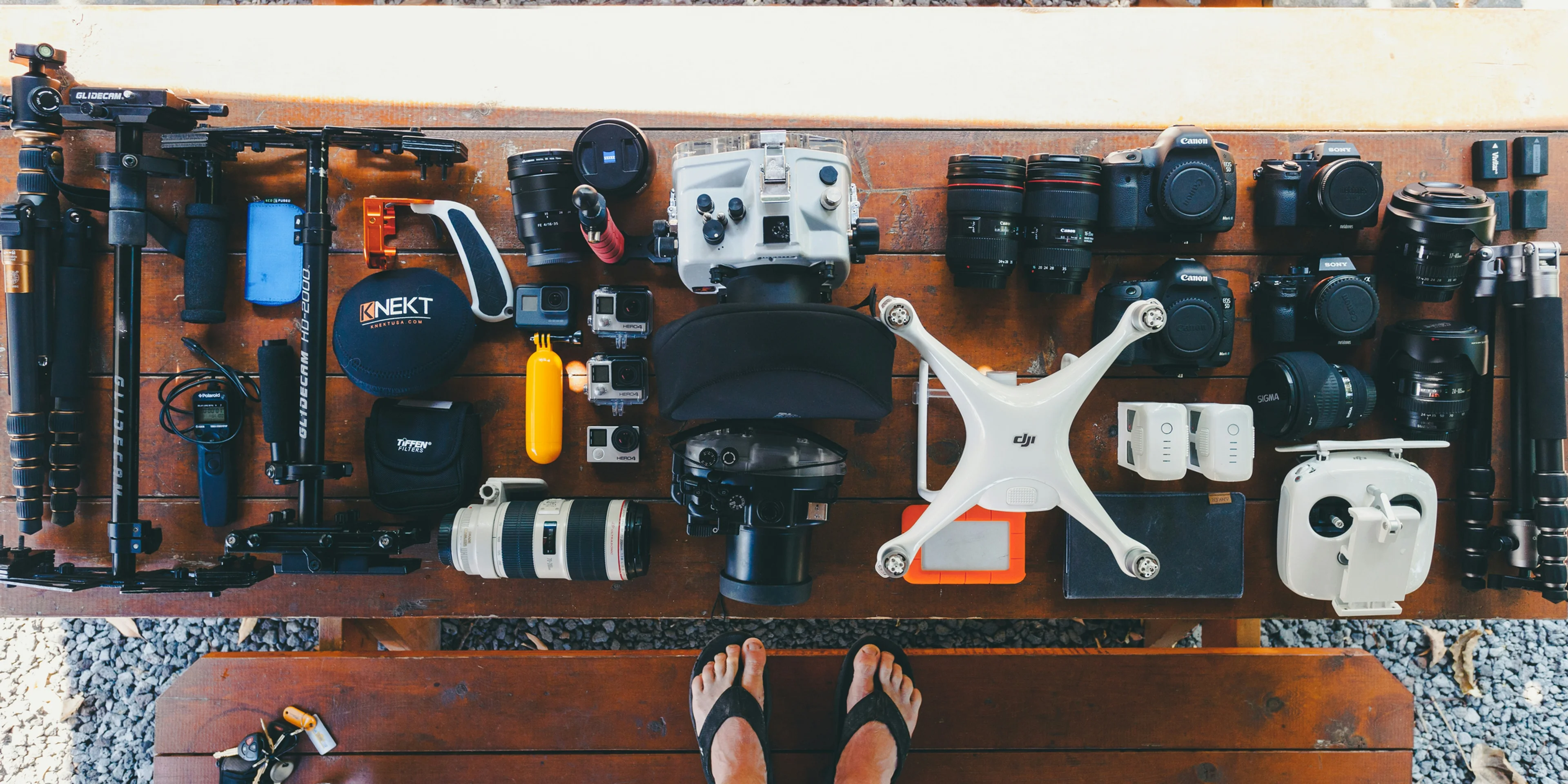 person standing near black and white quadcopter drone near cameras on brown wooden table.