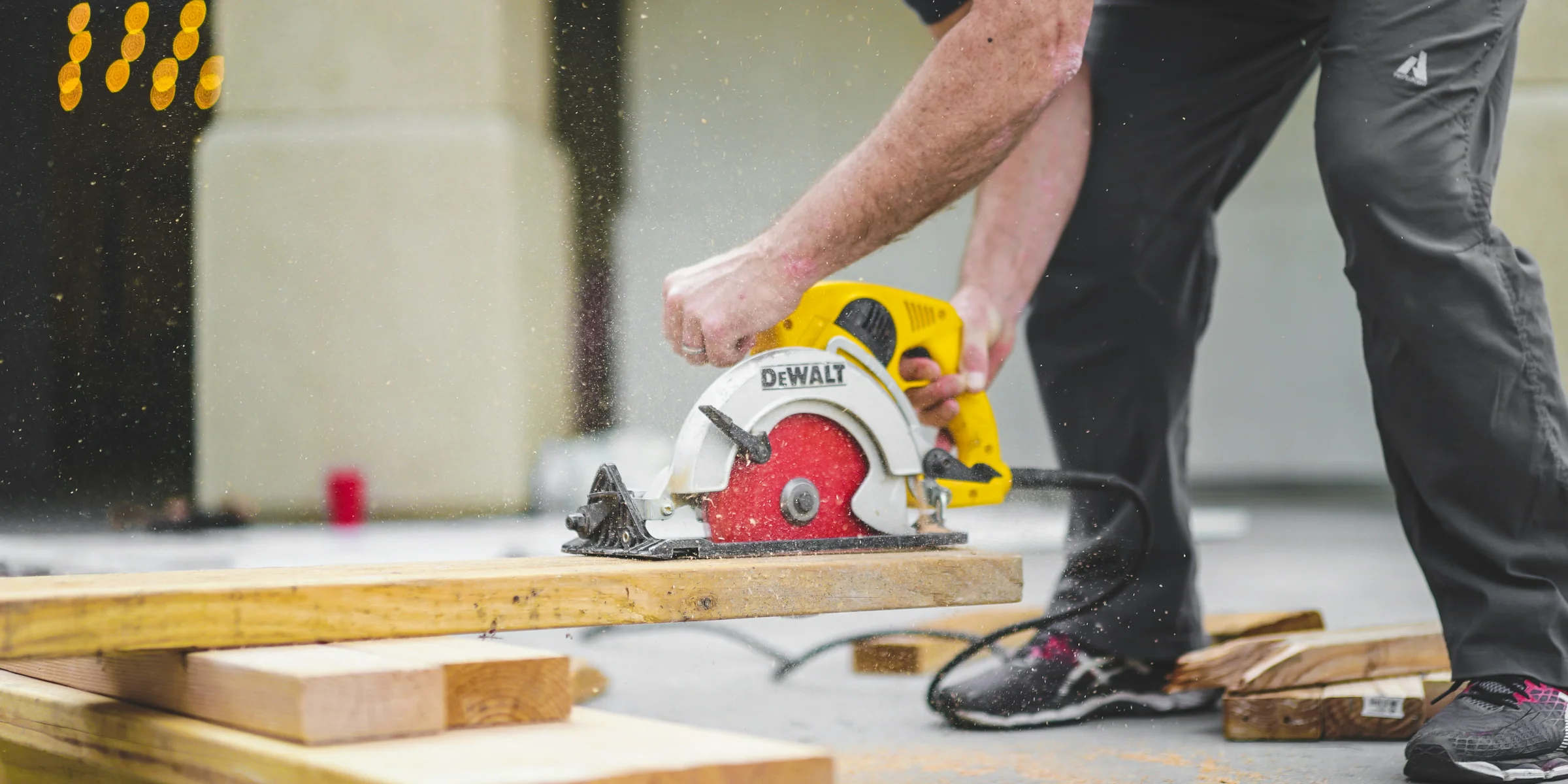 man in black sweatpants using DEWALT circular saw and cutting a wood plank.