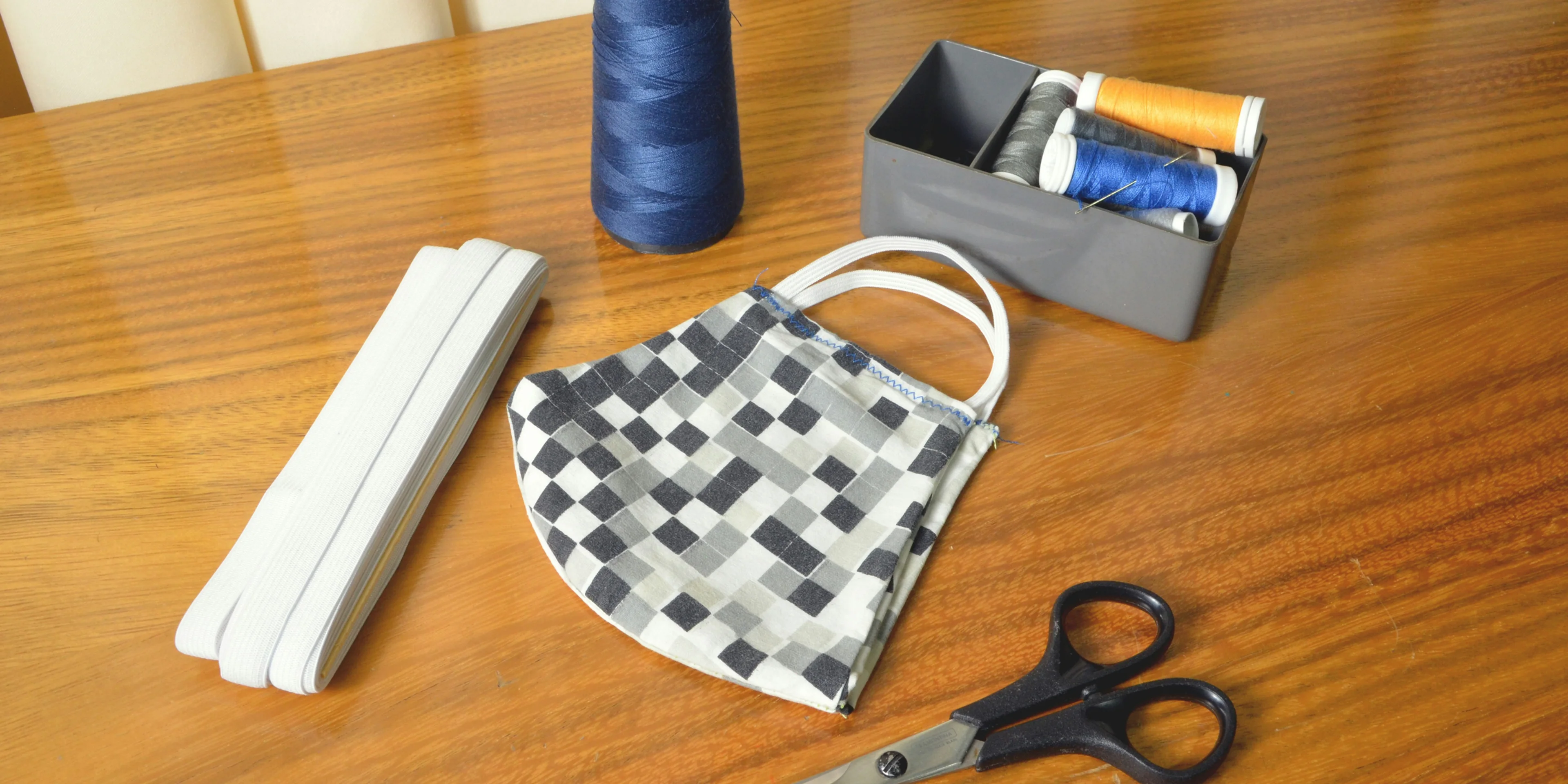 black handled scissors beside blue thread and white and black checkered pouch.