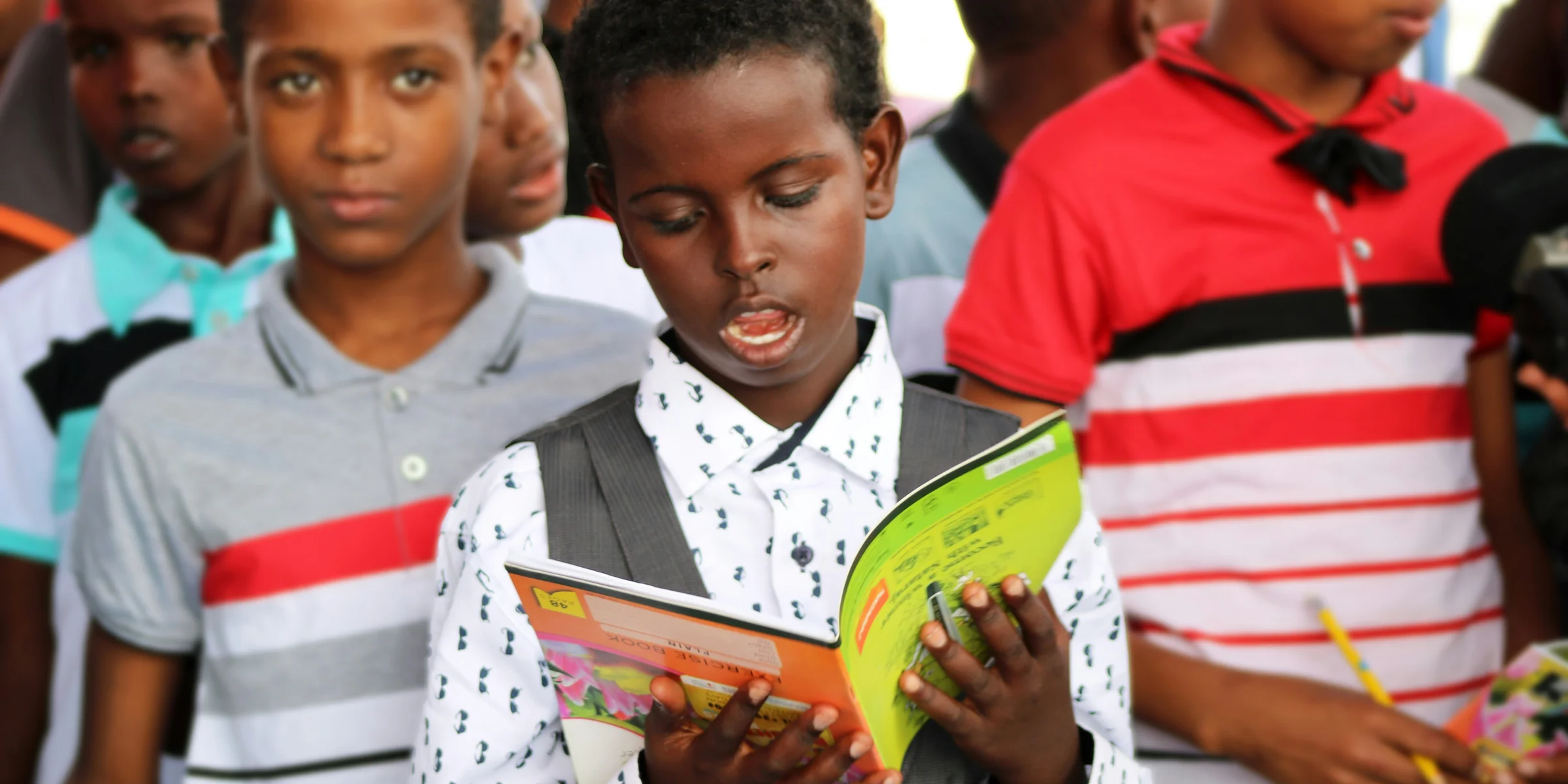 man in red and white polo shirt holding yellow book.