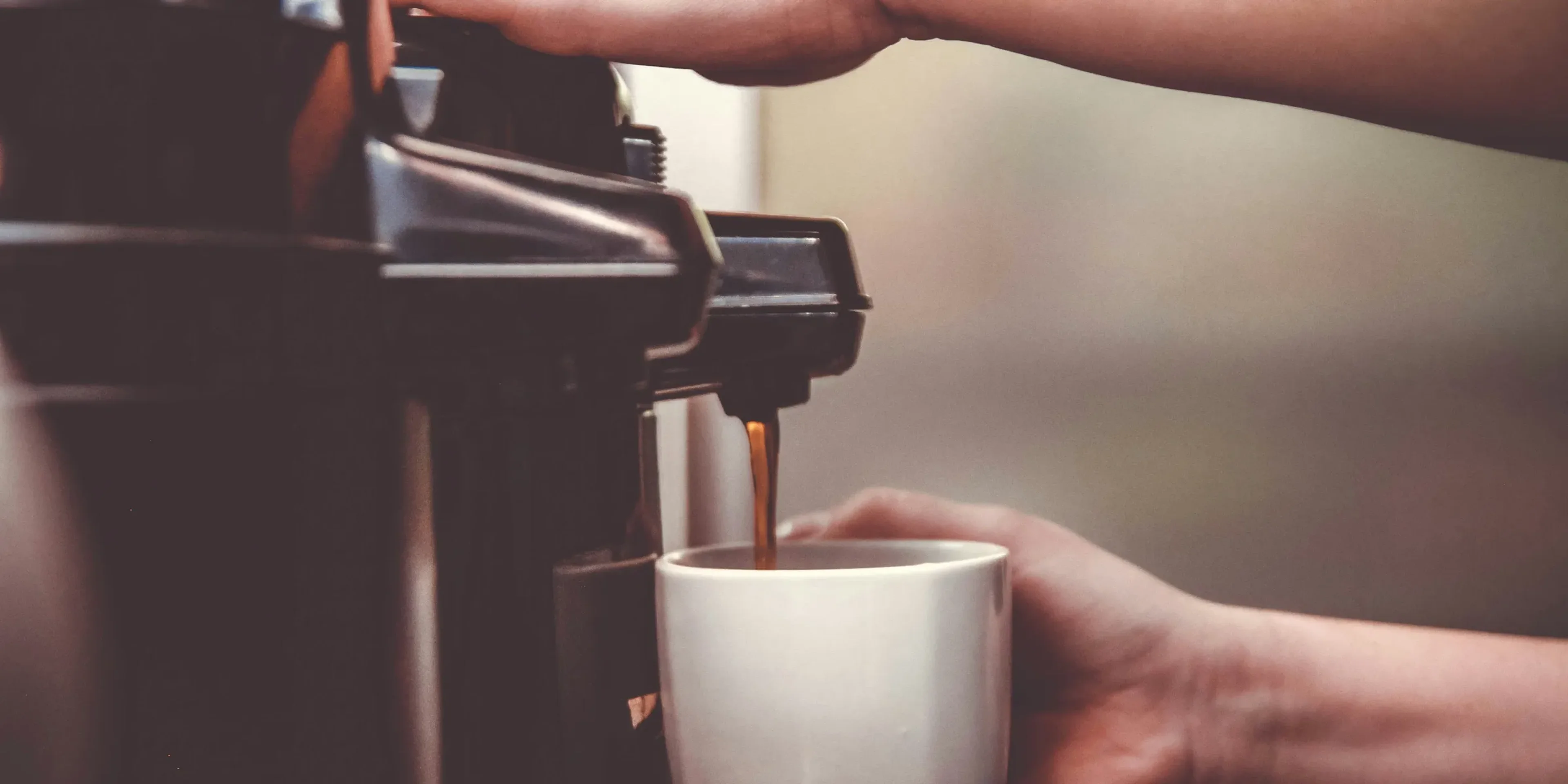 person using coffeemaker with white ceramic mug