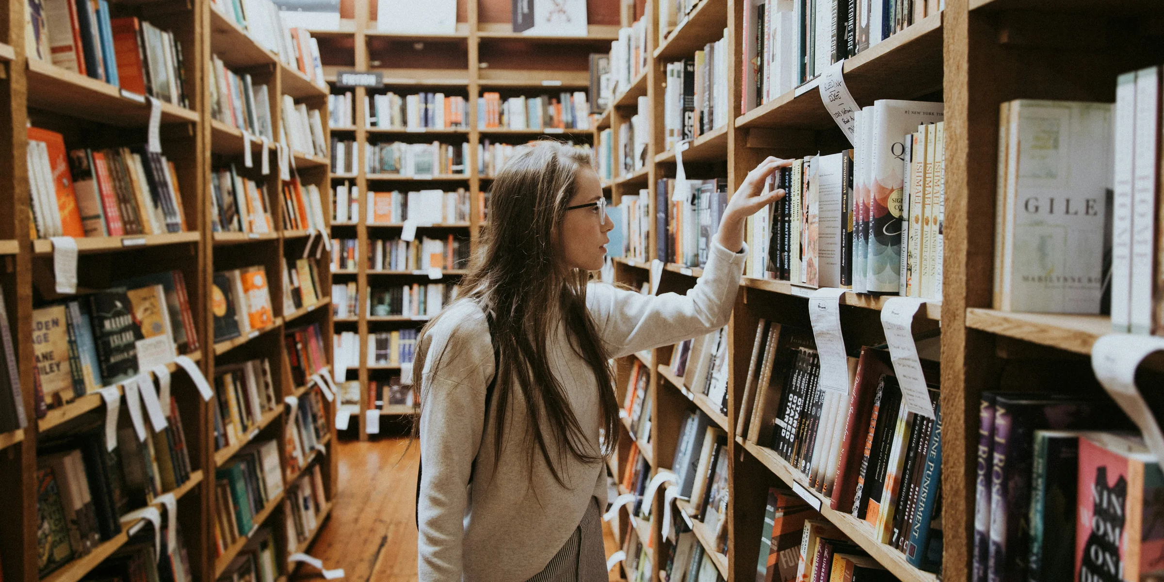 woman holding book on bookshelves