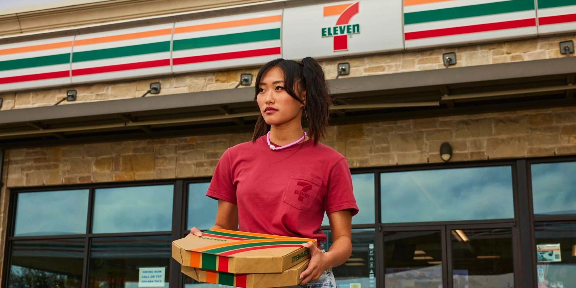 Person holding 2 pizza boxes outside of a 7-Eleven