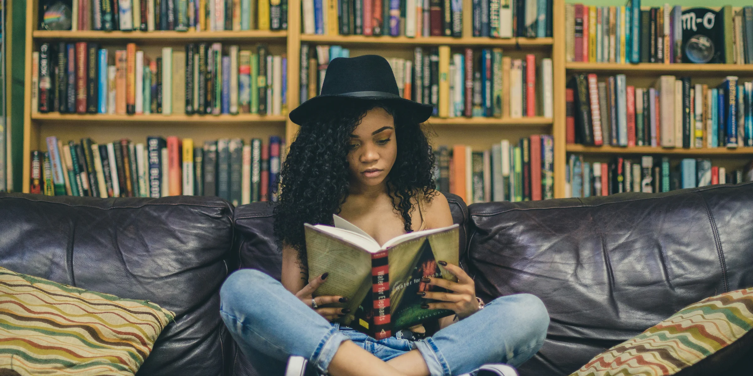 woman reading a book while sitting on black leather 3-seat couch.