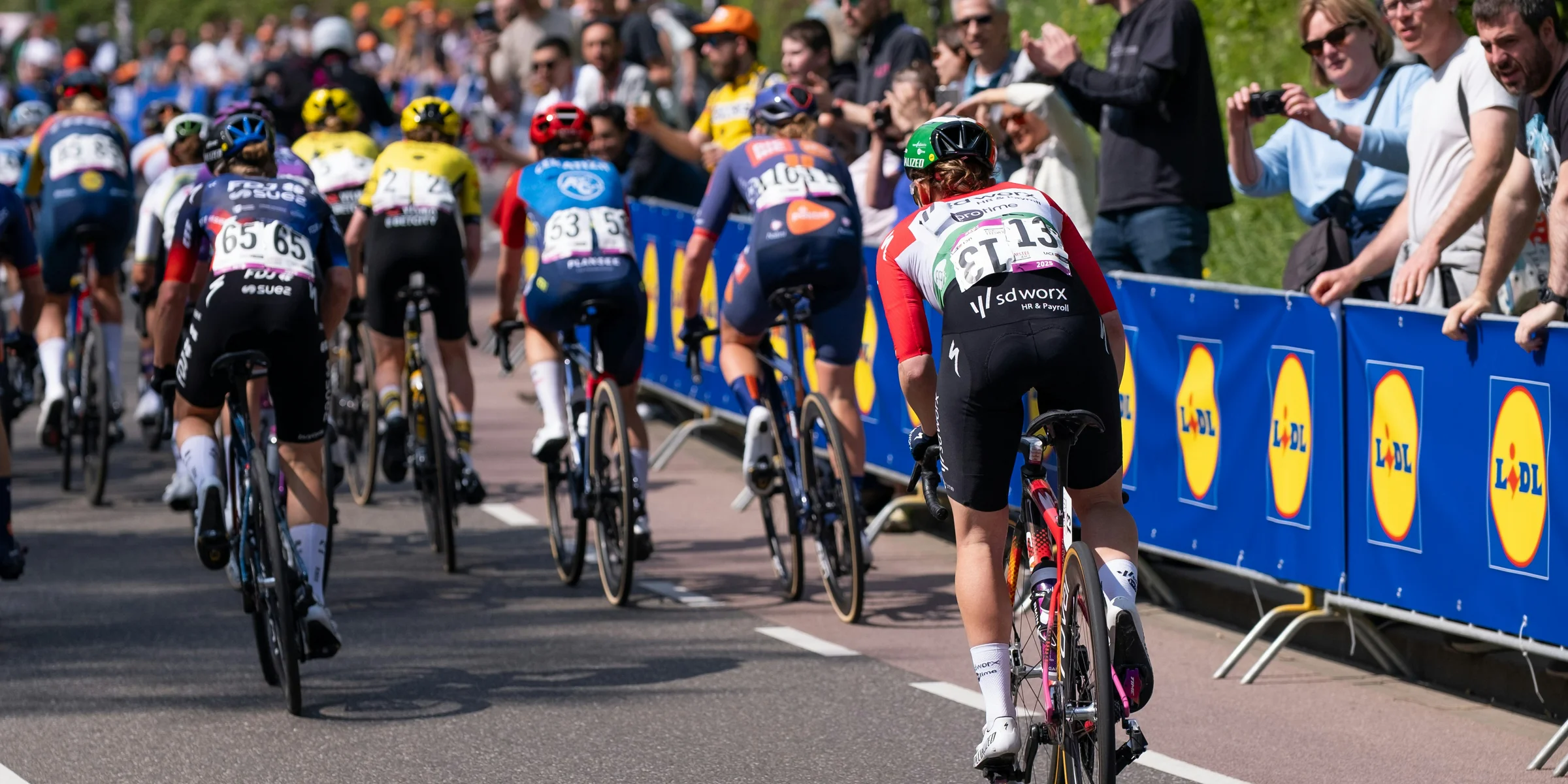 Cyclists race down a road with spectators watching.