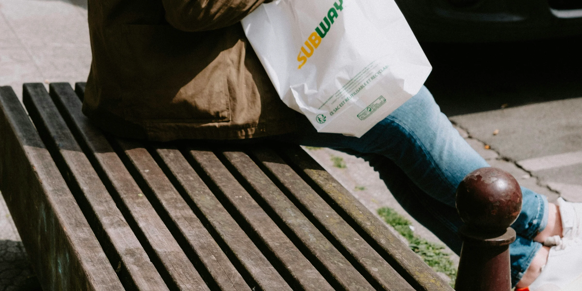 a person sitting on a bench with a bag of food.