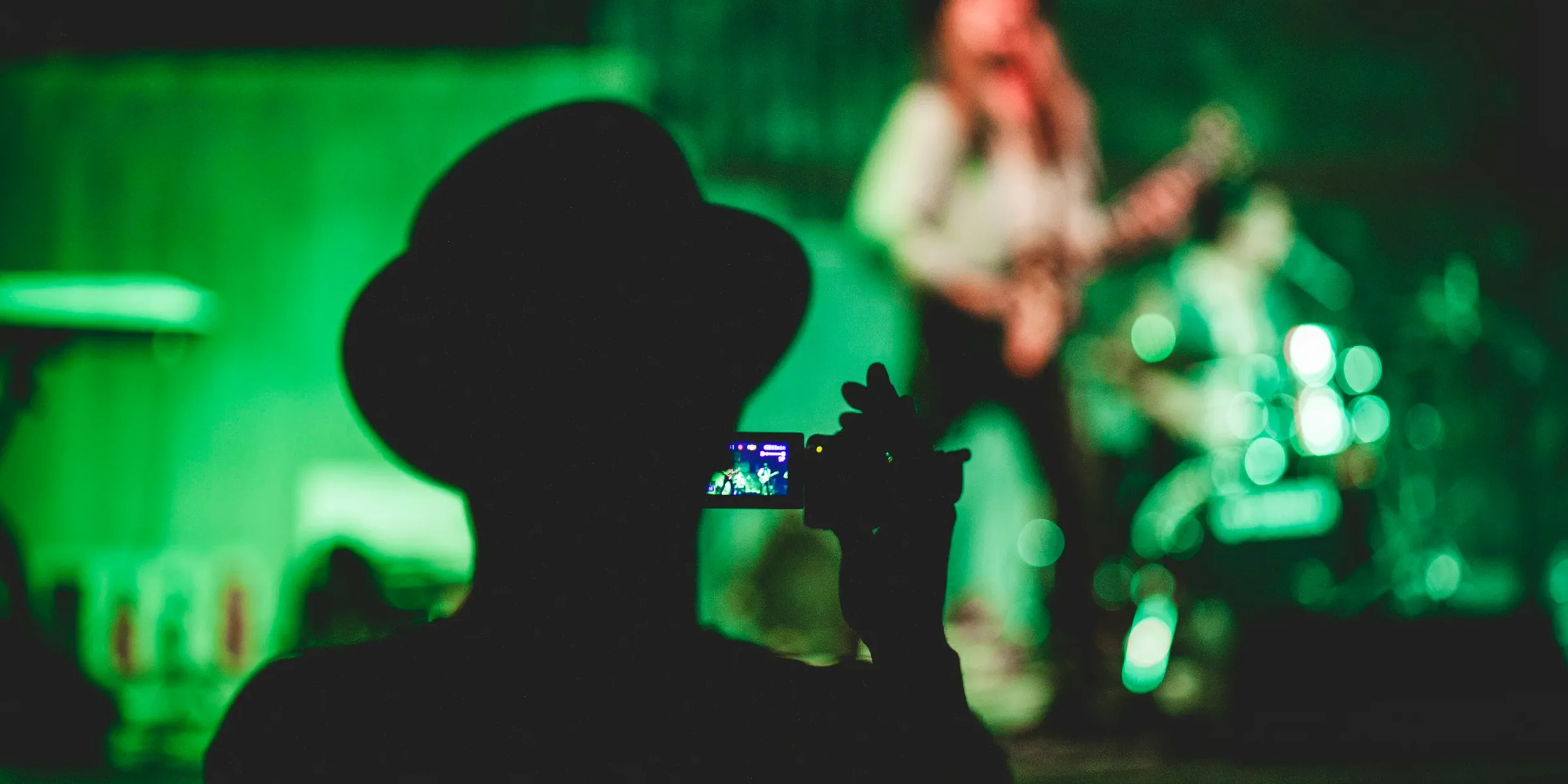 silhouette of man holding camcorder near woman singing on stage