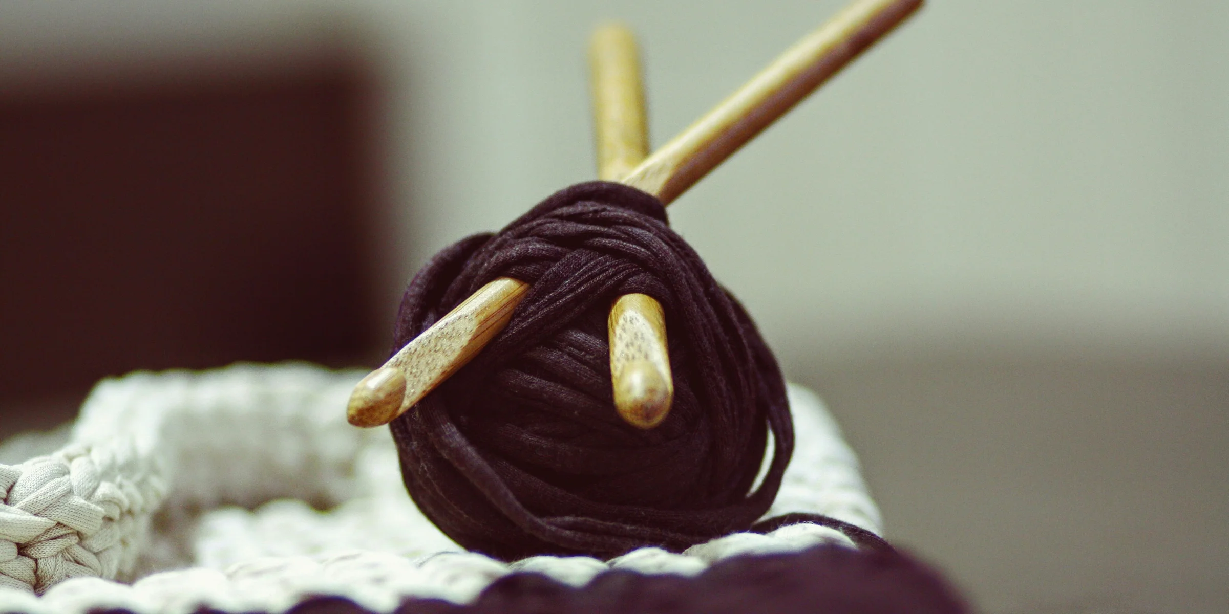 brown yarn roll with two brown crochet hooks on top of white surface.