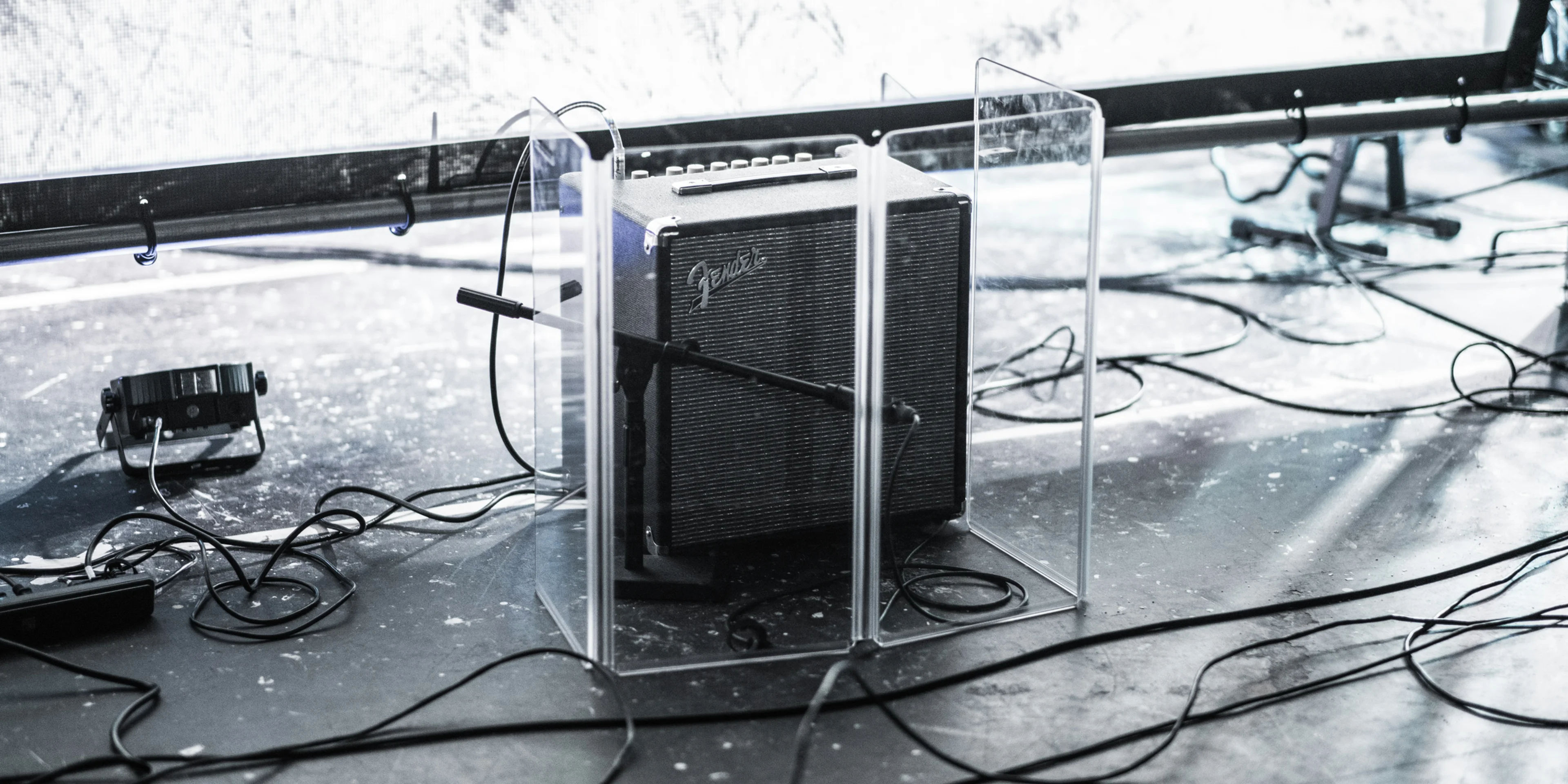 square gray and black Fender guitar amplifier enclosed by clear glass panel on top of stage beside stage lighting.