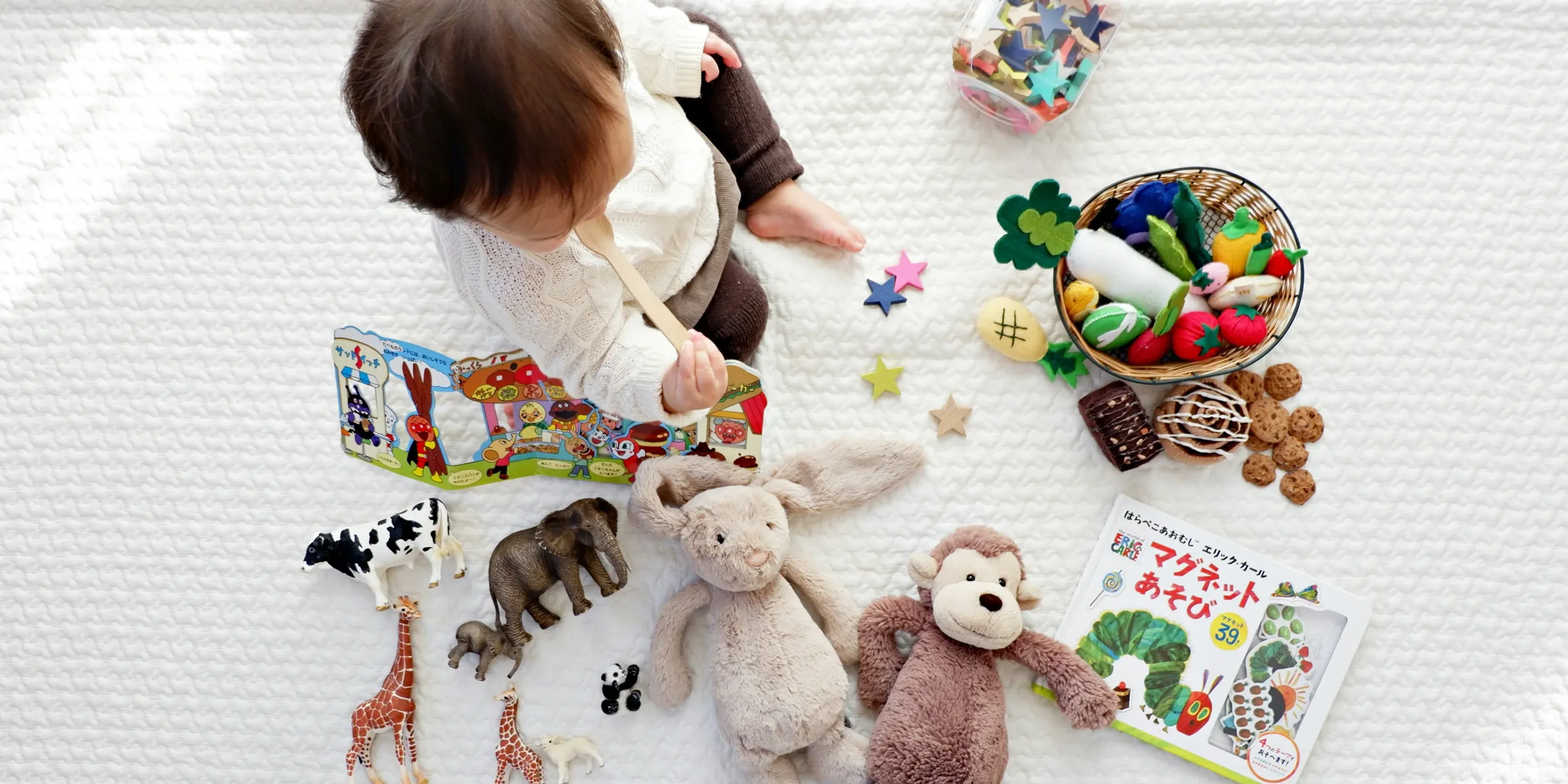 boy sitting on white cloth surrounded by toys