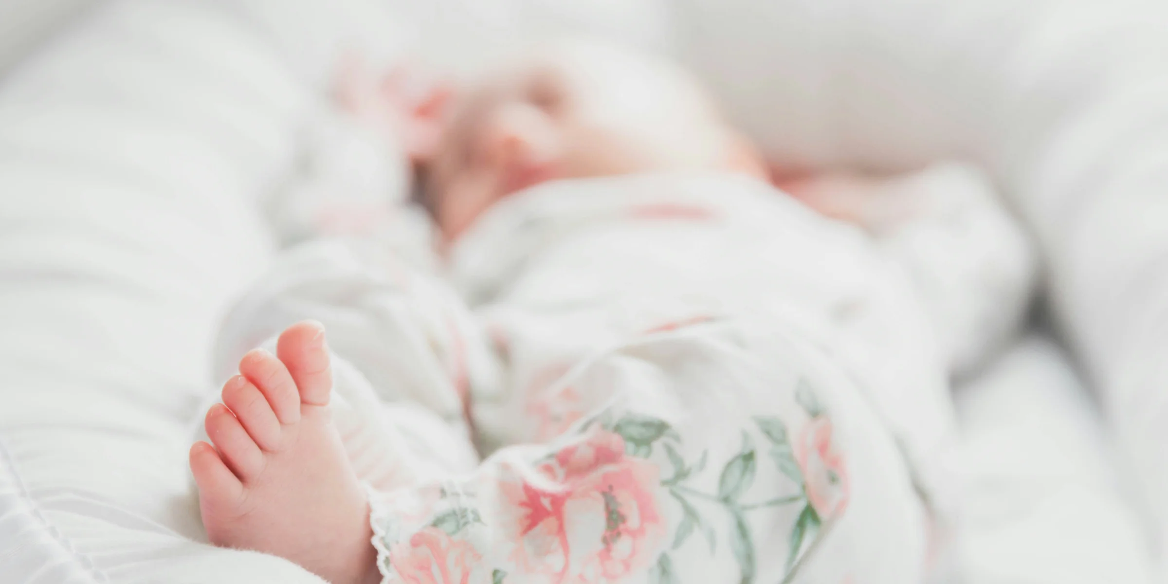 baby in white and red floral onesie lying on bed.