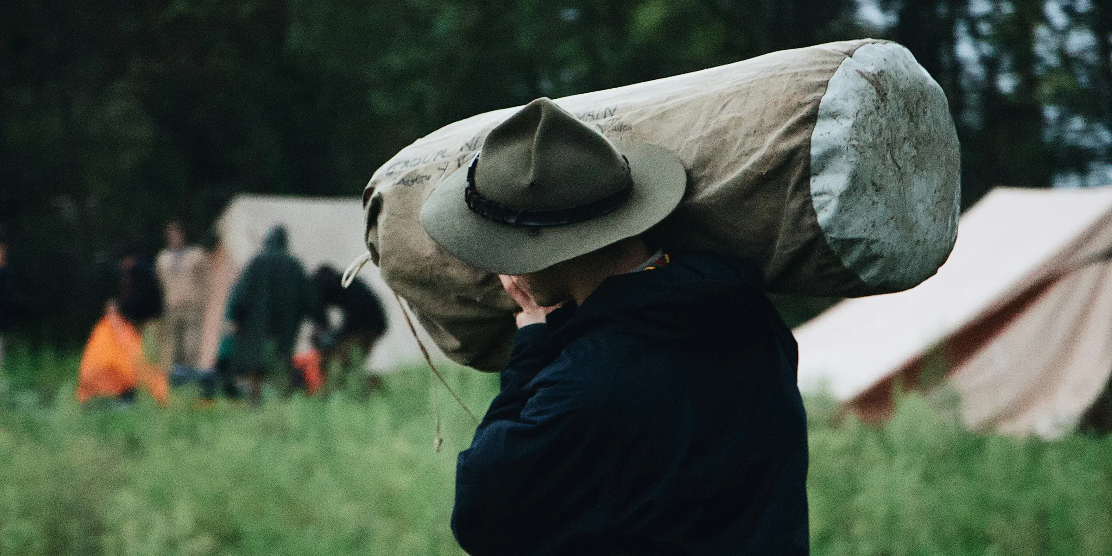 selective focus photography of walking man carrying bag near set-up tent