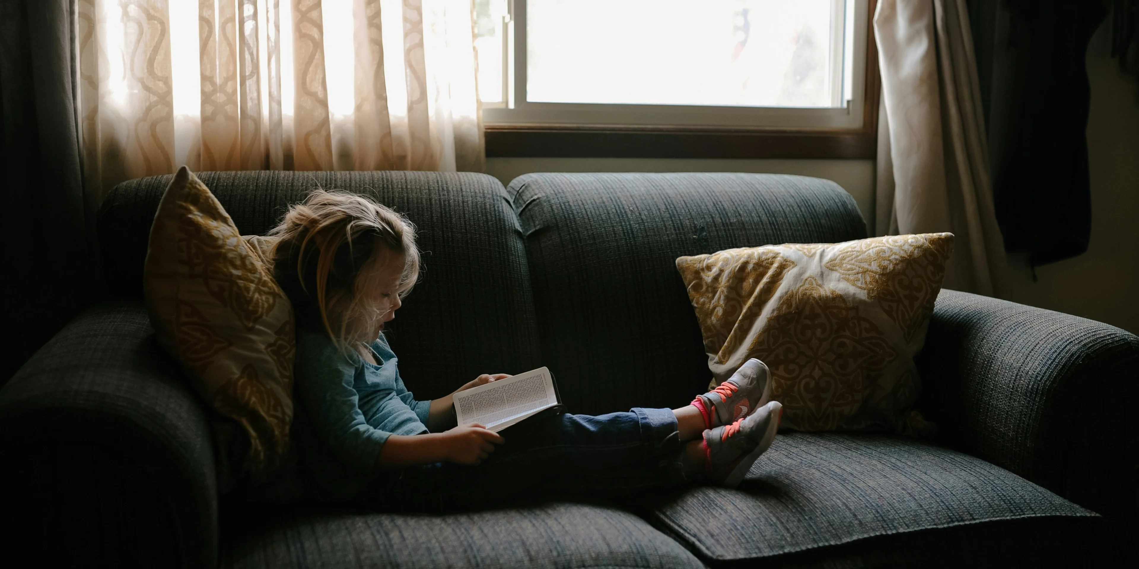 girl reading book sitting on sofa.