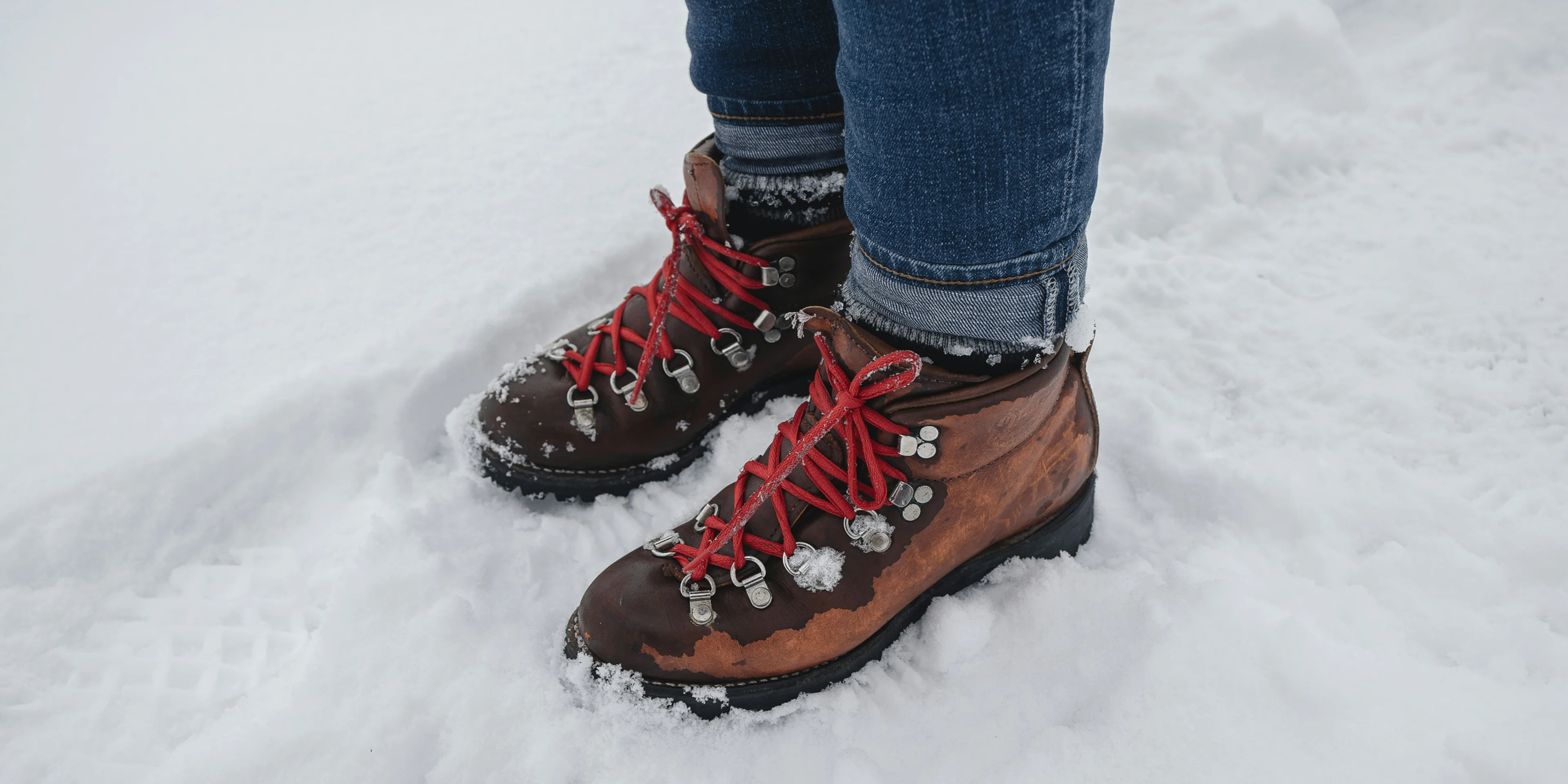 person in blue denim jeans and brown leather boots standing on snow covered ground during daytime.