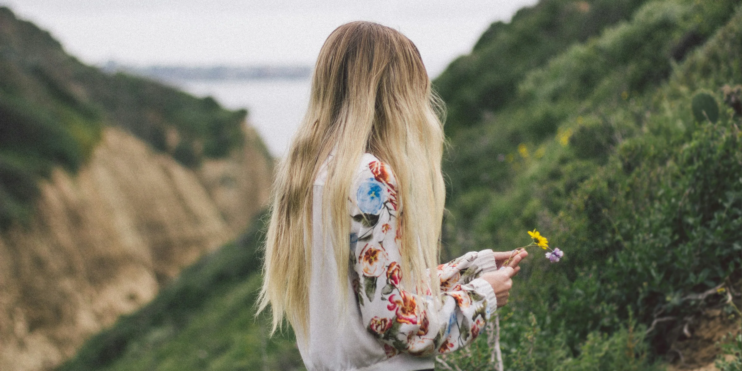 woman wearing white, green, and red floral long-sleeved shirt standing on green leaf plant covered hillside during daytime