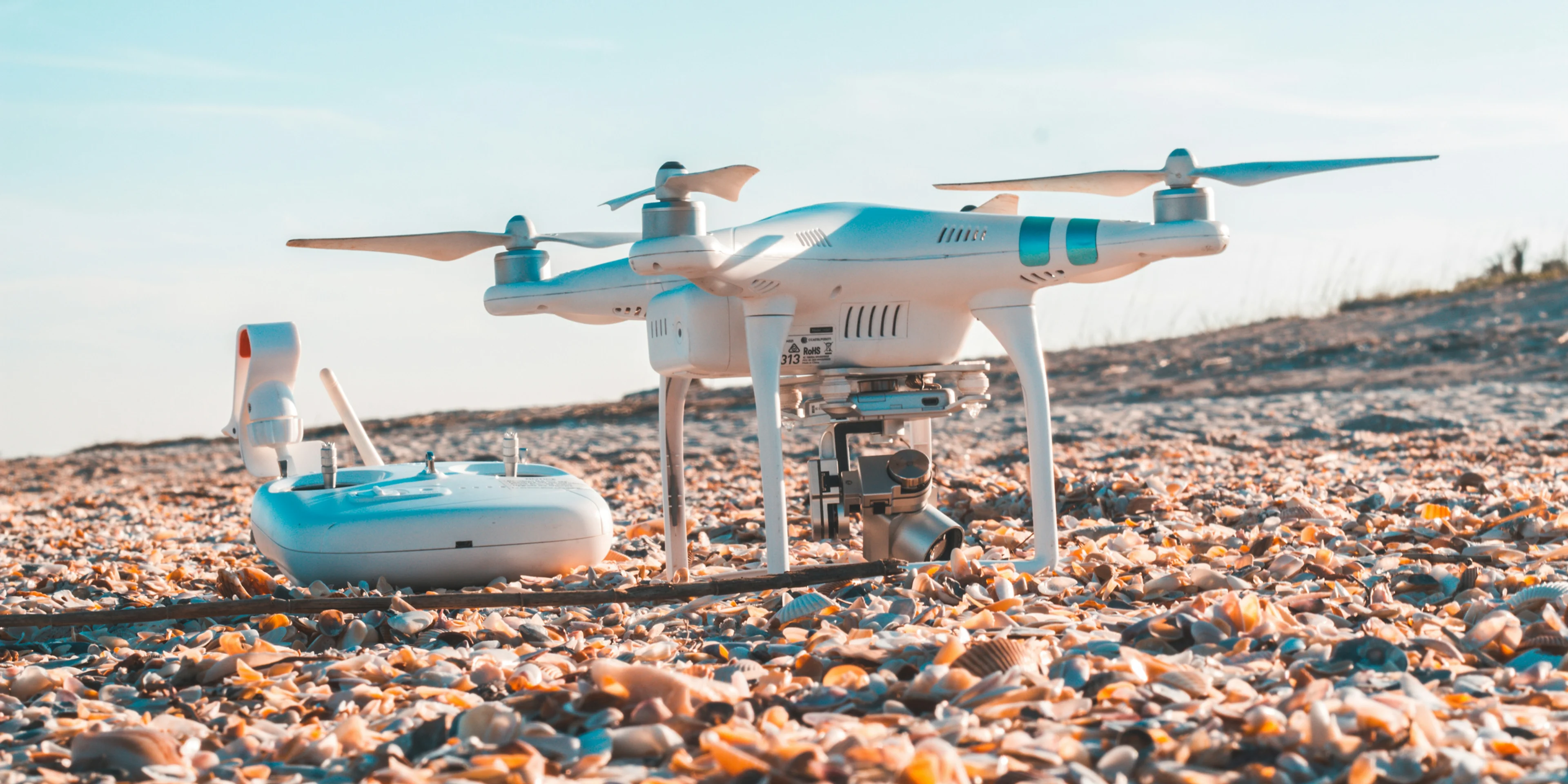 white DJI quadcopter and radio controller on rocky land.